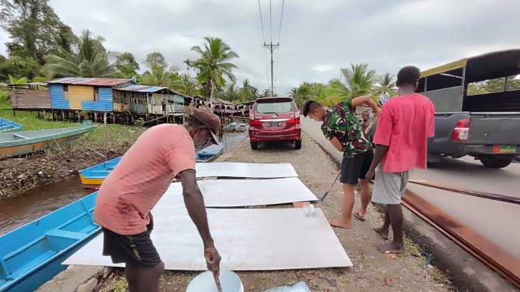 Pengecatan lembaran triplek yang akan digunakan sebagai plafon salah satu rumah sasaran. (Foto: NM)